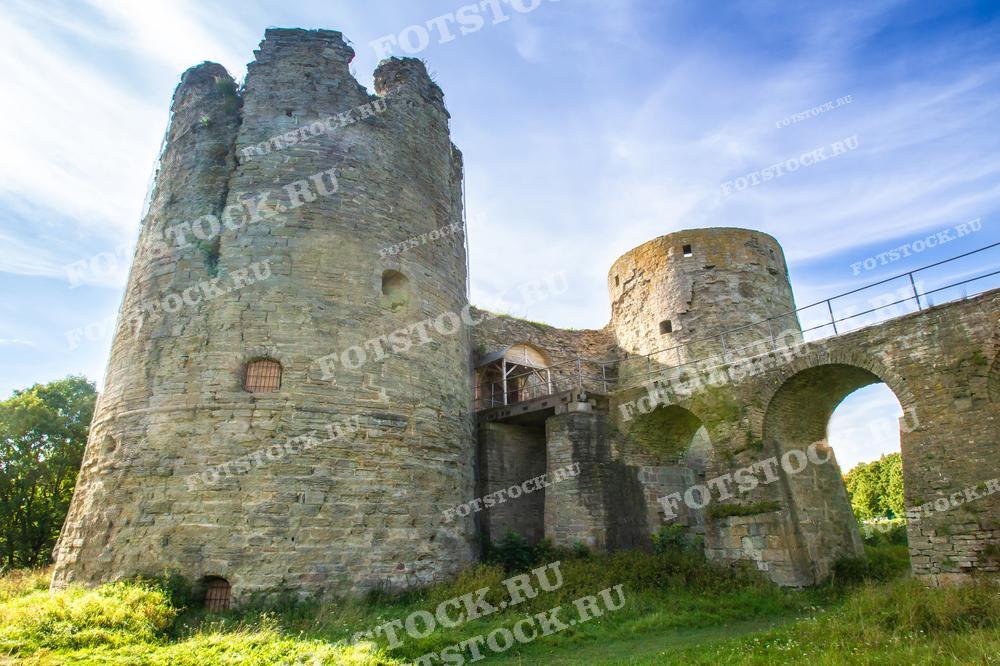 На фото изображены башни крепости Копорье в Ленинградской области. Видны старинные каменные стены, арочные мосты и элементы средневековой архитектуры. Это фото подойдет для использования в исторических материалах, туристических путеводителях и образовательных публикациях о Ленинградской области и Санкт-Петербурге.